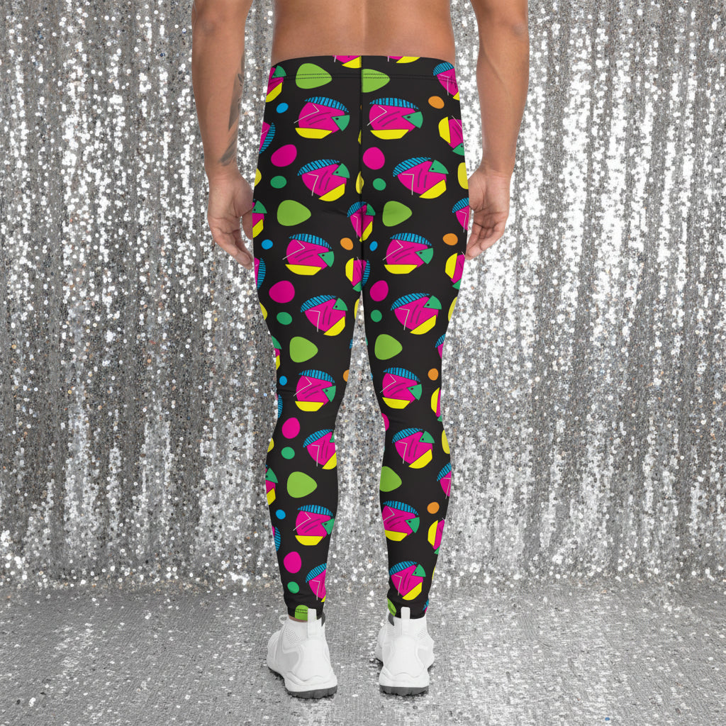Man from the waist down wearing men's Funk Party funky festival yoga leggings standing facing away with his hands by his sides. The man is standing on a blue gym or yoga may on a wooden floor in an apartment with light streaming in from large windows to the right. The funk party pattern is an abstract pattern in vibrant pink, orange, yellow, green and blue in a spotty type arrangement on a black background