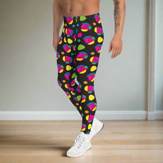 Man from the waist down wearing men's Funk Party funky festival yoga leggings standing facing to the left with his hands by his sides. The man is standing on a wooden floor in an apartment with light grey walls. The funk party pattern is an abstract pattern in vibrant pink, orange, yellow, green and blue in a spotty type arrangement on a black background