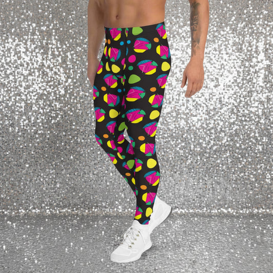 Man from the waist down wearing men's Funk Party funky festival yoga leggings standing facing to the left with his hands by his sides. The man is standing on a wooden floor in an apartment with light grey walls. The funk party pattern is an abstract pattern in vibrant pink, orange, yellow, green and blue in a spotty type arrangement on a black background