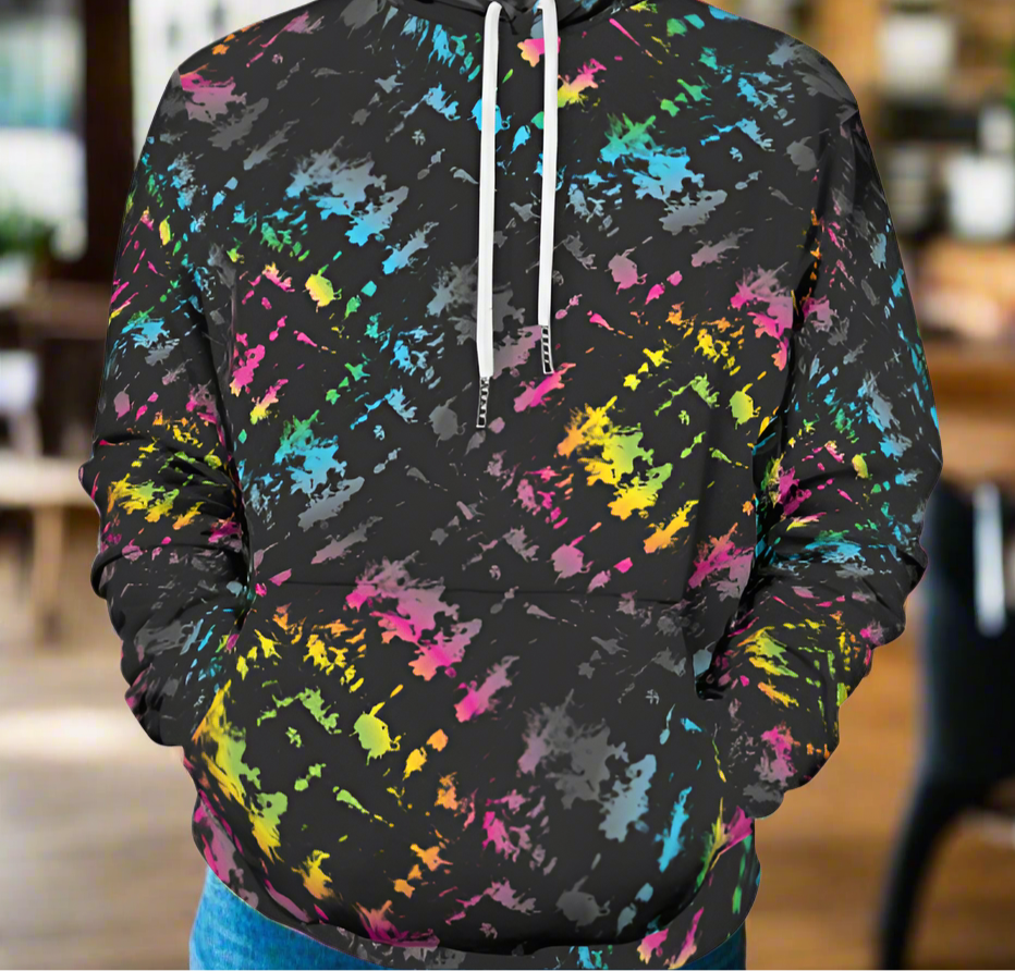 Man from the shoulders down to the waist, posing standing facing forwards wearing a 100% cotton vibrant Minstrel Magic tie-dye all-over print hoodie. He is standing in a rustic boho cafe.. The hoodie is black with splashes of bright pink, orange yellow, green, blue and grey. It is a bold fun design for everyday wear.