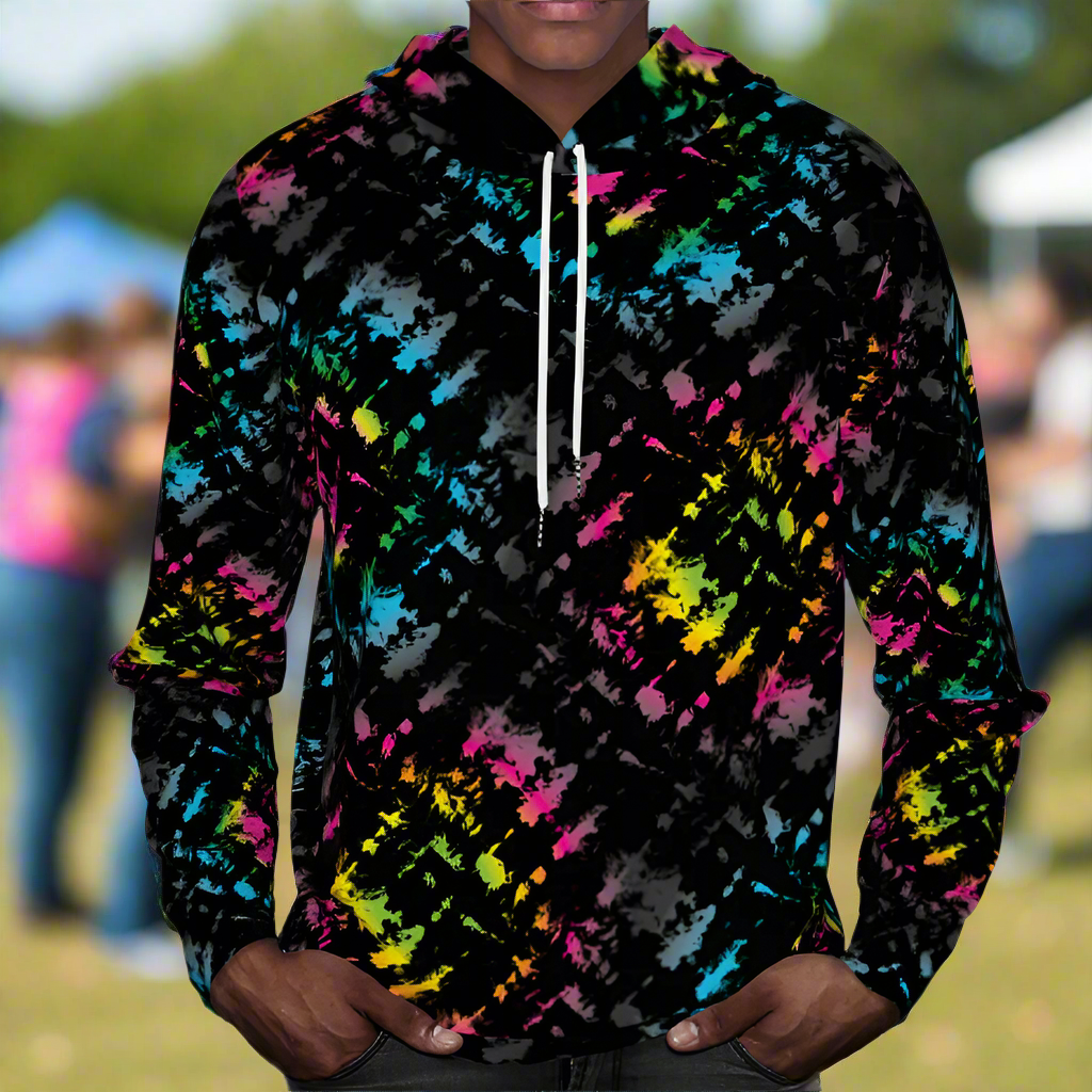 Man from the chin down to the waist, posing standing facing forwards wearing a 100% cotton vibrant Minstrel Magic tie-dye all-over print hoodie. He is standing outside at a public festival market. The hoodie is black with splashes of bright pink, orange yellow, green, blue and grey. It is a bold fun design for everyday wear.