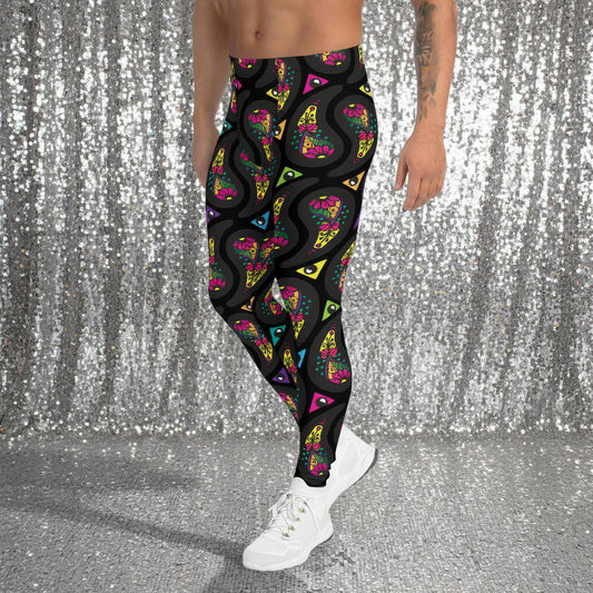 Man from the waist down wearing men's black paisley party funky festival yoga leggings standing facing to the left with his hands by his sides. He is wearing white trainers and is standing on a countryside green marked tennis court with trees in the background. The paisley party pattern is a colourful repeating large paisley pattern, made up of vibrant colours including pink, orange, yellow, green, blue and purple. In between the paisley print are colourful triangles in the same colours.