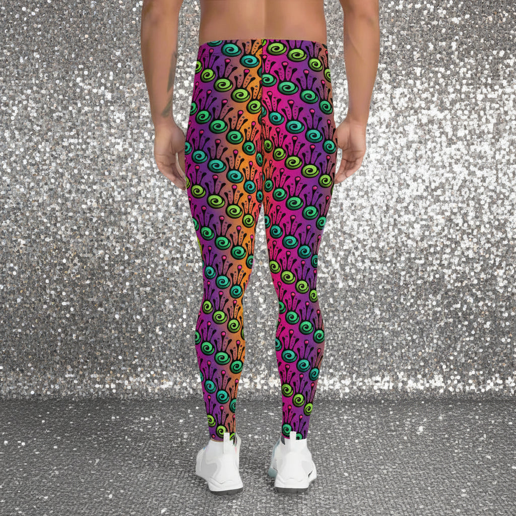 Man from the waist down wearing men's fire tribal frog funky festival yoga leggings standing facing away with his hands by his sides. He is wearing white trainers and is standing in a grassy festival field with other festival goers and market gazebos in the background. It is a sunny day. The fire tribal frog pattern is a funky abstract pattern with a blended pink, purple and orange background.
