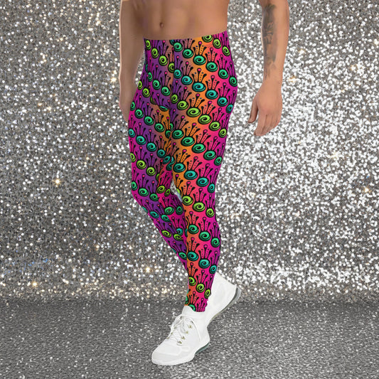 Man from the waist down wearing men's fire tribal frog funky festival yoga leggings standing facing to the left with his hands by his sides. He is wearing white trainers and is standing in a grassy festival field with other festival goers mingling in the background. It is a sunny day. The fire tribal frog pattern is a funky abstract pattern with a blended pink, purple and orange background.