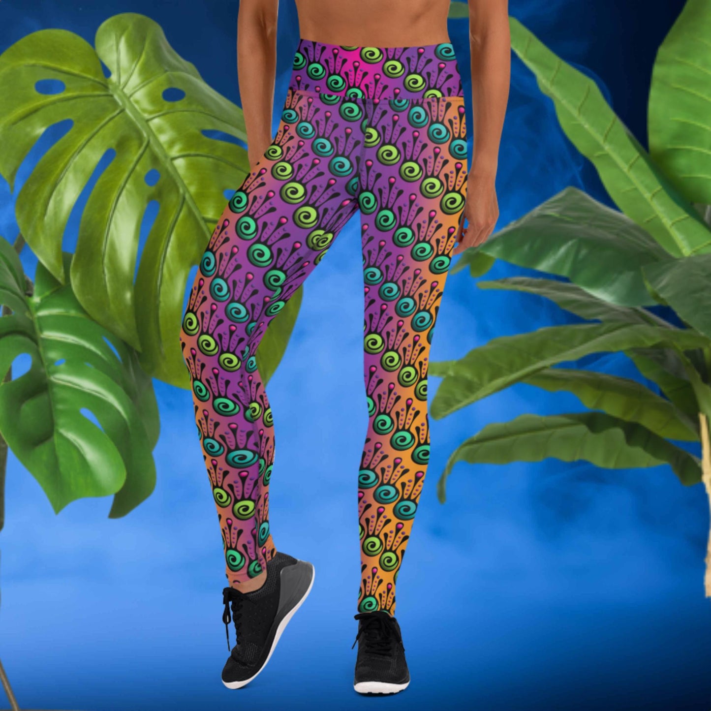 Woman from the waist down wearing high-waist Tribal Frog funky festival yoga leggings standing facing forwards with her hands by her sides. The woman is standing in front of a smoky blue background in front of two large leafy plants. The fire tribal frog pattern is an abstract pattern with a blended purple, pink and orange background.