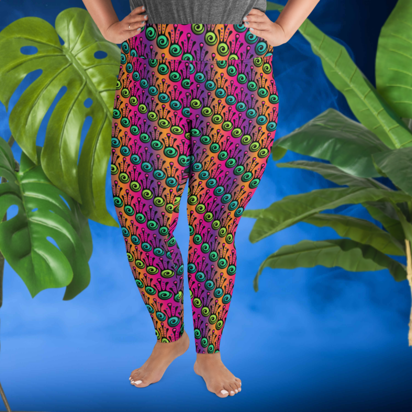 A curvy woman from the waist down wearing plus-size high-waist Tribal Frog funky festival yoga leggings standing facing forwards with both of her hands on her hips. The woman is standing in front of a smoky blue background in front of two large leafy plants. The fire tribal frog pattern is an abstract pattern with a blended purple, pink and orange background.