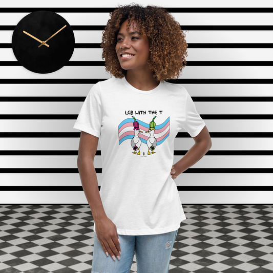Woman standing facing forwards and looking to the left, wearing a fitted white Sassy Seagull LGB with the T LGBTQ+ Pride T-Shirt and pale stonewash blue jeans. She is standing in a black and white theme space with horizontal stripes on the wall and a black clock on the wall. The t-shirt is white with short sleeves. The graphic shows two cartoon style seagulls wearing colourful hats walking away in front of an trans flag, underneath the wording LGB with the T. It is a soft playful design for everyday wear