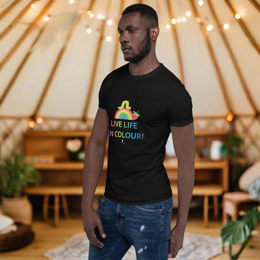 Man wearing a black 100% cotton vibrant, rainbow live life in colour t-shirt in a bohemian yurt interior decorated with fairy lights, rugs, candles and plants.