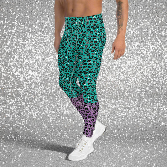 Man from the waist down wearing mens Purple and Green Leopard Glamour funky festival yoga leggings standing facing to the left with his hands by his sides. The man is standing in a park in spring with pink and yellow tulips flowering and trees in the background. This design features an animal print pattern in black, grey and white, printed at a medium scale. The top 3/4 background is mint green with the bottom 1/4 purple