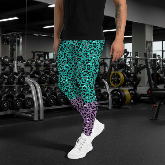 Man from the waist down wearing mens Purple and Green Leopard Glamour funky festival yoga leggings standing facing to the left with his hands by his sides. The man is standing in a park in spring with pink and yellow tulips flowering and trees in the background. This design features an animal print pattern in black, grey and white, printed at a medium scale. The top 3/4 background is mint green with the bottom 1/4 purple