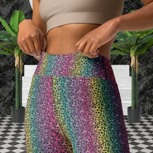 Close up of a woman from the chest down to her thighs wearing high-waist Rainbow Leopard Glamour funky festival yoga leggings standing facing forwards. The woman is standing on a black and white tiled floor in front of some white steps and a black and grey marble background. There is a leafy plant on the floor at each side of the steps. The rainbow leopard glamour design is an animal print pattern in black, grey and white, printed at a small scale against a blended rainbow background