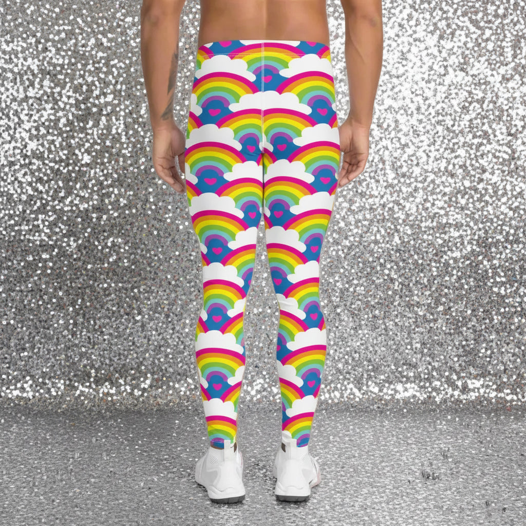 Man from the waist down wearing men's Rainbow Love funky festival yoga leggings standing facing away with his hands by his sides. The man is standing on a dance floor with colourful stage light either side of him in red and green which are reflected on the floor. The background is hazy mixed with glow from the coloured lights. The rainbow love pattern features repeating rainbows and white fluffy clouds with a small pink heart beneath each rainbow. The background colour is royal sky blue