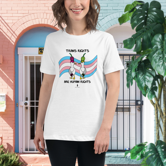Woman standing facing forwards wearing a Sassy Seagull Trans Rights Are Human Rights fitted t-shirt.She is standing in front of pink and blue houses with white doors. The t-shirt is white with short sleeves. The graphic shows two cartoon style seagulls wearing colourful hats walking away in front of a trans pride flag. The words Trans Rights sit above the image and below the words: Are Human Rights.