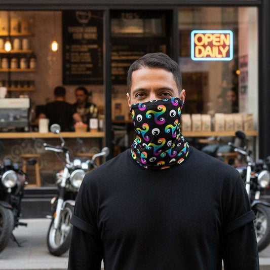 Man wearing a Trippy Triskelion neck gaiter as a face covering with a motorcycle cafe in the background and motorbikes parked outside.