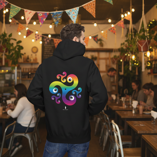 Man facing away wearing a black Trippy Triskelion hoodie with a rainbow-coloured, Celtic-inspired design on the back with a psychedelic twist. He is standing in a cosy boho cafe filled with plants and wooden tables.
