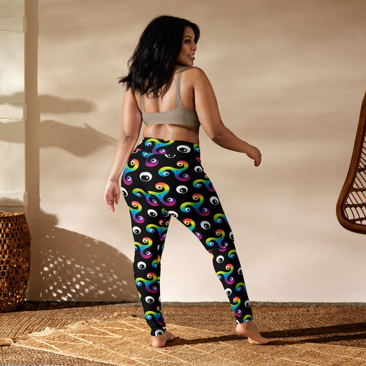 Curvy woman wearing black and rainbow trippy Triskelion leggings and a sports bra in a sunlit room facing away