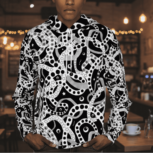 Man from the chin down to the waist, posing standing facing forwards wearing a 100% cotton bold black and white Who's Afraid Of The Dark all-over print hoodie. He is standing against a stage background with lights and smoke effects. The hoodie has an abstract design made up of interwoven shapes detailed with spots, stars and lines. It is a unique and bold design for everyday wear.
