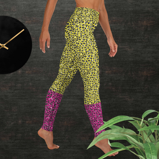 Woman from the waist down wearing high-waist Yellow and Pink Leopard Glamour funky festival yoga leggings standing facing right with her hands by her sides. The woman is standing in front of a textured grey background with a black and gold wall clock to the left and a partially visible leafy plant on the floor in the bottom right. This design features an animal print pattern in black, grey and white, printed at a medium scale. The top 3/4 background is bright yellow with the bottom 1/4 a hot pink colour