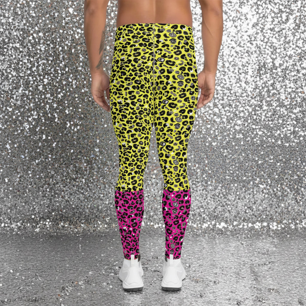 Man from the waist down wearing mens Yellow and Pink Leopard Glamour funky festival yoga leggings standing facing away with his hands by his sides. The man is wearing white trainers and standing outside at a festival after dark with other festival goers and lights in the background. This design features an animal print pattern in black, grey and white, printed at a medium scale. The top 3/4 background is bright yellow with the bottom 1/4 bright pink