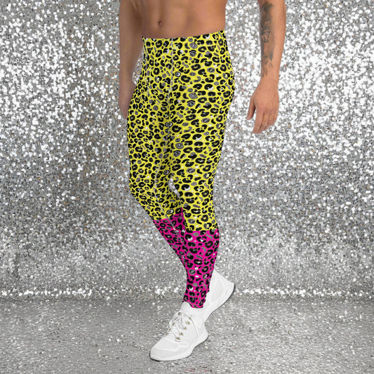 Man from the waist down wearing mens Yellow and Pink Leopard Glamour funky festival yoga leggings standing facing to the left with his hands by his sides. The man is wearing white trainers and standing outside at a festival after dark with other festival goers and lights in the background. This design features an animal print pattern in black, grey and white, printed at a medium scale. The top 3/4 background is bright yellow with the bottom 1/4 bright pink