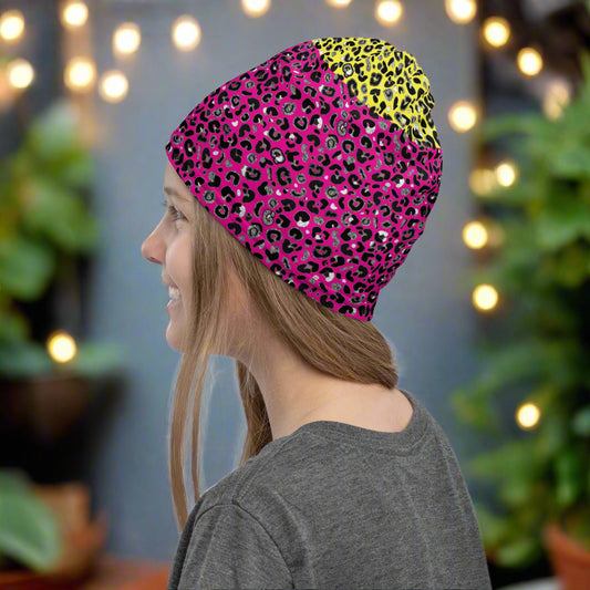 Girl with long dark blonde hair facing to the left wearing a grey top and a vibrant yellow and pink neck gaiter as a beanie hat. In the background are some fairy lights and plants. This design features an animal print pattern in black, grey and white, printed at a medium scale. The top 3/4 background is bright yellow with the bottom 1/4 a hot pink colour. In this image, the pink is the dominant colour