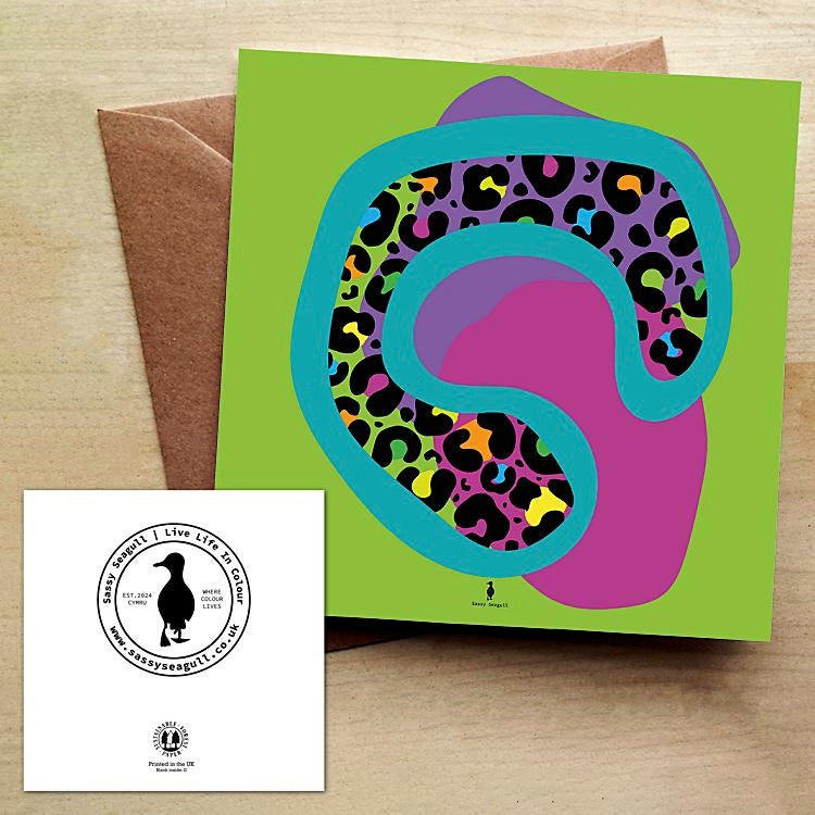 Colorful abstract animal print design on a green card with a brown envelope on a wooden table.