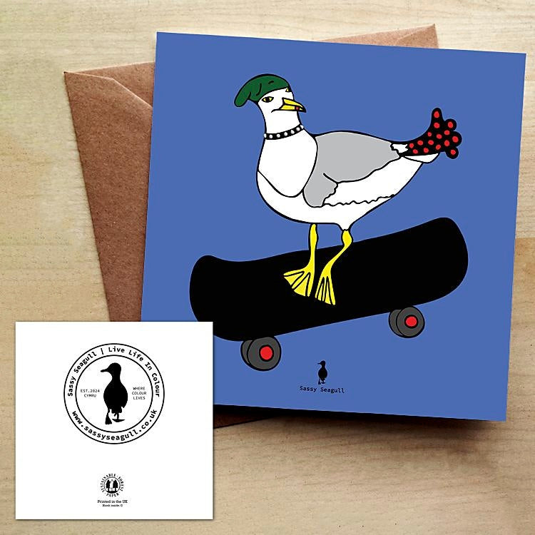 Blue greeting card featuring an illustrated seagull on a skateboard, with a brown envelope on a wooden table.