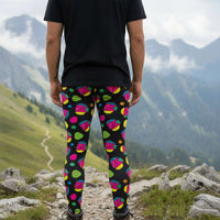 Man from the waist down wearing men's Funk Party funky festival yoga leggings standing facing away with his hands by his sides. The man is standing on a blue gym or yoga may on a wooden floor in an apartment with light streaming in from large windows to the right. The funk party pattern  is an abstract pattern in vibrant pink, orange, yellow, green and blue in a spotty type arrangement on a black background