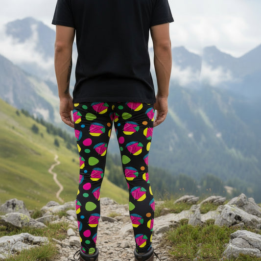 Man from the waist down wearing men's Funk Party funky festival yoga leggings standing facing away with his hands by his sides. The man is standing on a blue gym or yoga may on a wooden floor in an apartment with light streaming in from large windows to the right. The funk party pattern  is an abstract pattern in vibrant pink, orange, yellow, green and blue in a spotty type arrangement on a black background