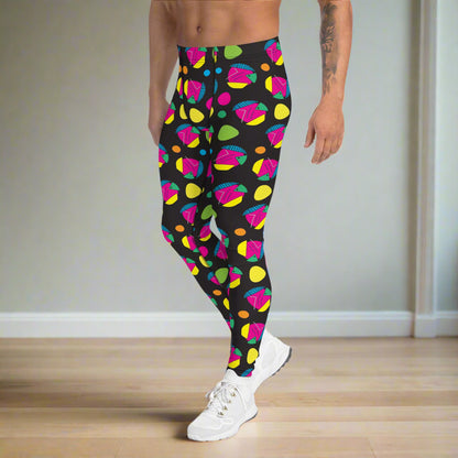 Man from the waist down wearing men's Funk Party funky festival yoga leggings standing facing to the left with his hands by his sides. The man is standing on a wooden floor in an apartment with light grey walls. The funk party pattern  is an abstract pattern in vibrant pink, orange, yellow, green and blue in a spotty type arrangement on a black background