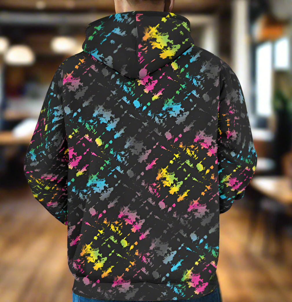 Man from the neck down to the waist, posing standing facing away wearing a 100% cotton vibrant Minstrel Magic tie-dye all-over print hoodie. He is standing in a rustic boho cafe.. The hoodie is black with splashes of bright pink, orange yellow, green, blue and grey. It is a bold fun design for everyday wear.