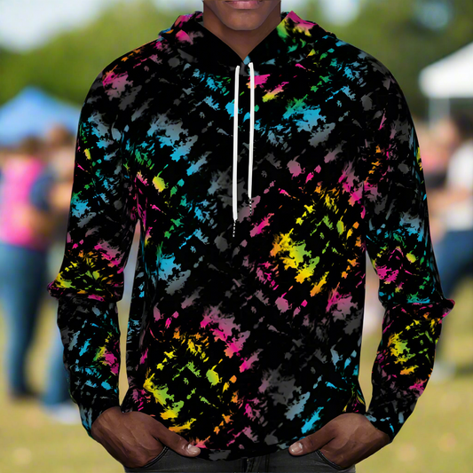 Man from the chin down to the waist, posing standing facing forwards wearing a 100% cotton vibrant Minstrel Magic tie-dye all-over print hoodie. He is standing outside at a public festival market. The hoodie is black with splashes of bright pink, orange yellow, green, blue and grey. It is a bold fun design for everyday wear.