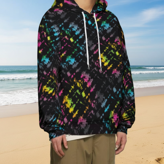 Man from the chin down to the waist, posing standing facing to the right wearing a 100% cotton vibrant Minstrel Magic tie-dye all-over print hoodie. He is standing outside amongst autumnal trees with golden leaves blanketing the ground. The hoodie is black with splashes of bright pink, orange yellow, green, blue and grey. It is a bold fun design for everyday wear.
