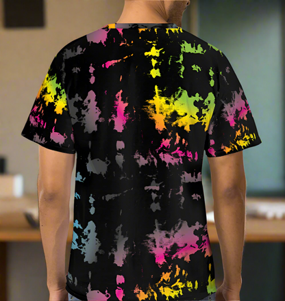 Man from the neck down to the waist, posing standing facing away wearing a 100% cotton vibrant minstrel magic tie-dye all-over print t-shirt. He is standing in  a rustic cafe environment. The t-shirt is black with splashes of bright pink, orange yellow, green, blue and grey. It is a bold fun design for everyday wear.