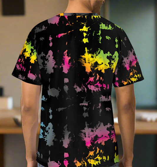 Man from the neck down to the waist, posing standing facing away wearing a 100% cotton vibrant minstrel magic tie-dye all-over print t-shirt. He is standing in  a rustic cafe environment. The t-shirt is black with splashes of bright pink, orange yellow, green, blue and grey. It is a bold fun design for everyday wear.
