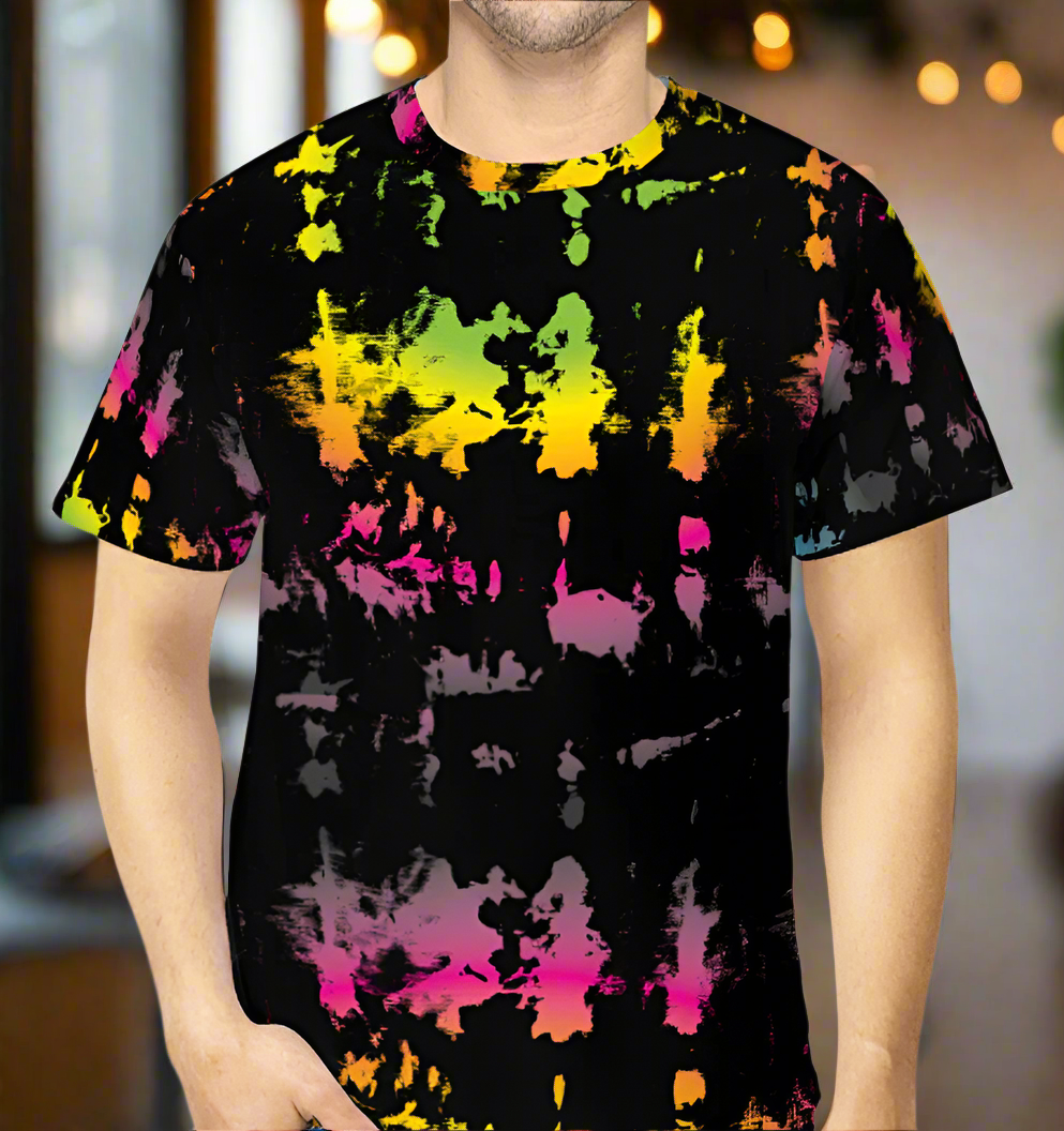 Man from the chin down to the waist, posing standing facing forwards wearing a 100% cotton vibrant minstrel magic tie-dye all-over print t-shirt. He is standing in  a rustic cafe environment. The t-shirt is black with splashes of bright pink, orange yellow, green and grey. It is a bold fun design for everyday wear.