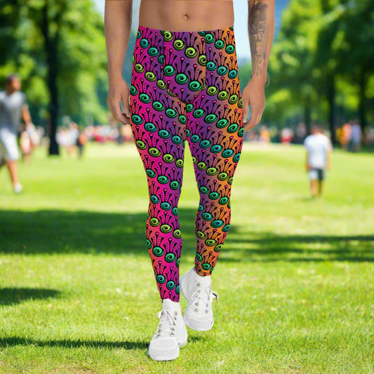 Man from the waist down wearing men's fire tribal frog funky festival yoga leggings standing facing forwards with his hands by his sides. He is wearing white trainers and is standing in a grassy park with trees and other walkers in the background. The fire tribal frog pattern  is a funky abstract pattern with a blended pink, purple and orange background.