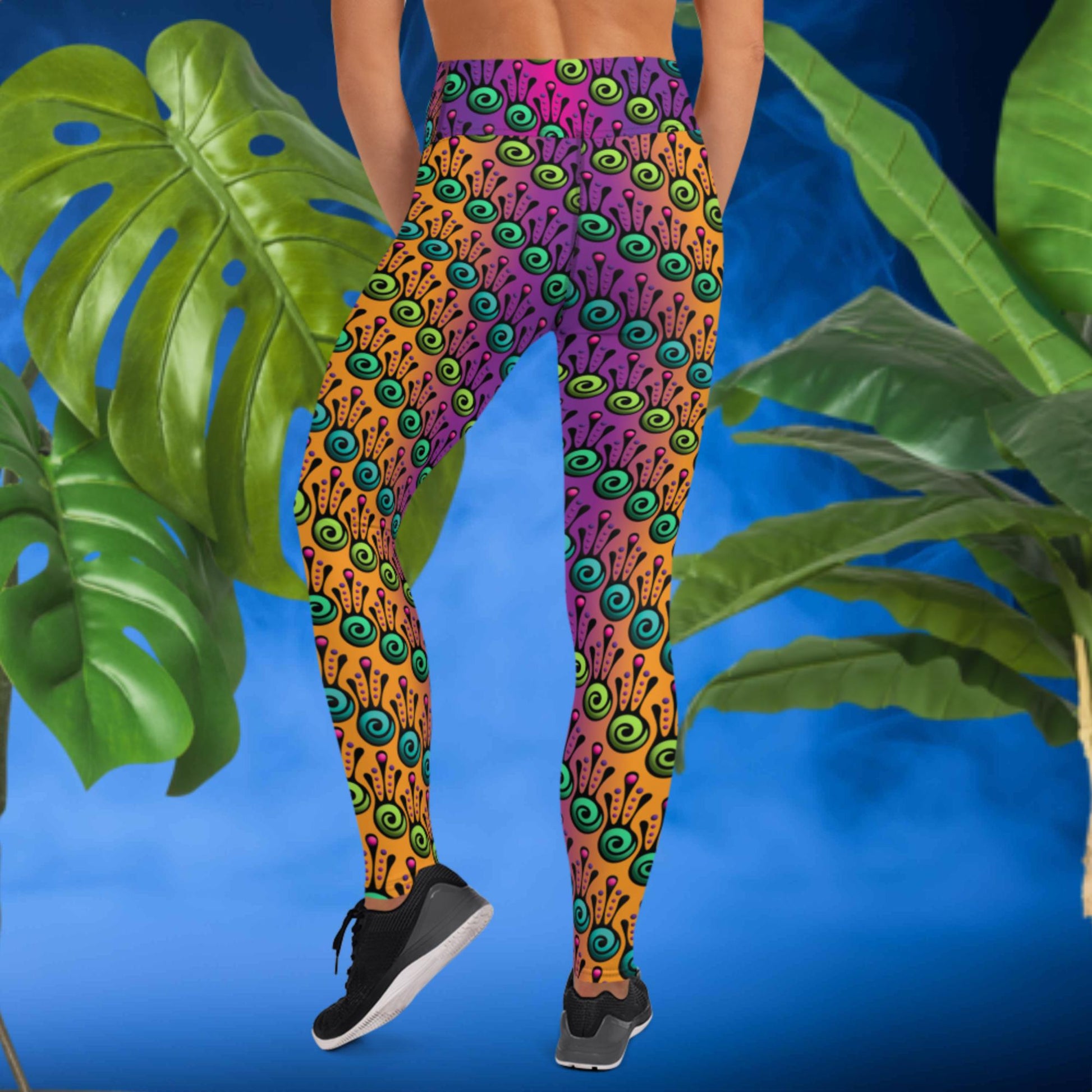 Woman from the waist down wearing high-waist Tribal Frog funky festival yoga leggings standing facing backwards with her hands by her front. The woman is standing in front of a smoky blue background in front of two large leafy plants. The fire tribal frog pattern is an abstract pattern with a blended purple, pink and orange background.