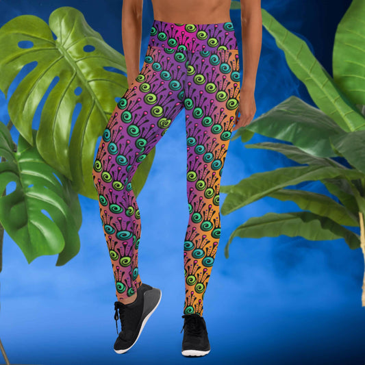 Woman from the waist down wearing high-waist Tribal Frog funky festival yoga leggings standing facing forwards with her hands by her sides. The woman is standing in front of a smoky blue background in front of two large leafy plants. The fire tribal frog pattern is an abstract pattern with a blended purple, pink and orange background.