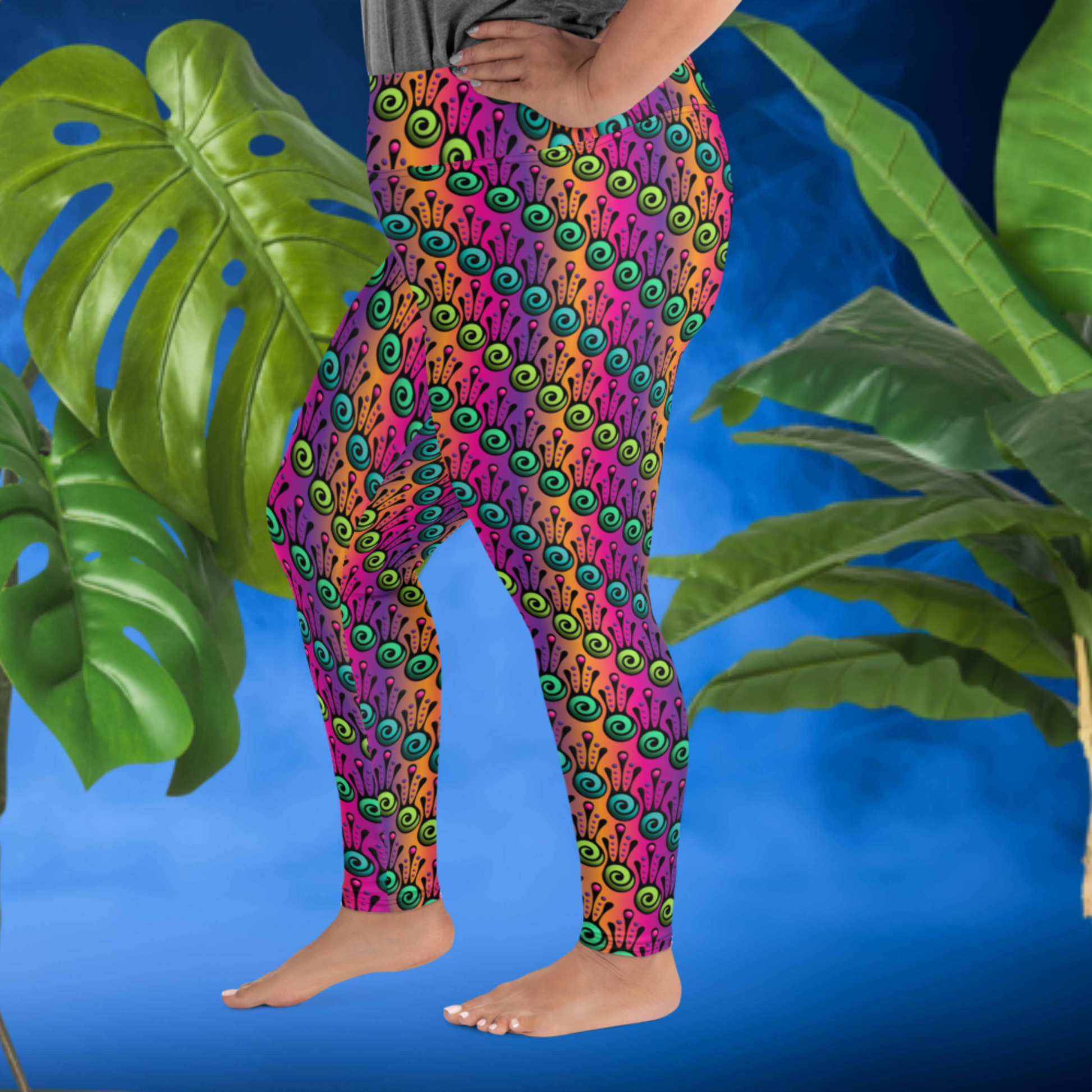 A curvy woman from the waist down wearing plus-size high-waist Tribal Frog funky festival yoga leggings standing facing to the left with her right foot forward and with both of her hands on her hips. The woman is standing in front of a smoky blue background in front of two large leafy plants. The fire tribal frog pattern is an abstract pattern with a blended purple, pink and orange background.