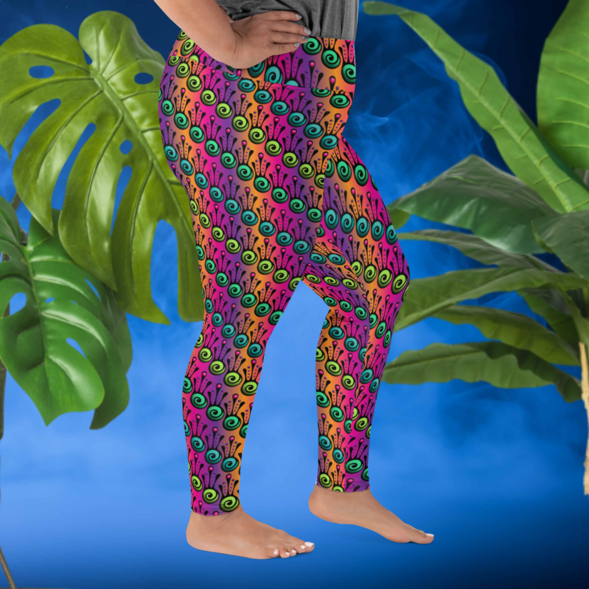 A curvy woman from the waist down wearing plus-size high-waist Tribal Frog funky festival yoga leggings standing facing to the right with her left foot forward and with both of her hands on her hips. The woman is standing in front of a smoky blue background in front of two large leafy plants. The fire tribal frog pattern is an abstract pattern with a blended purple, pink and orange background.