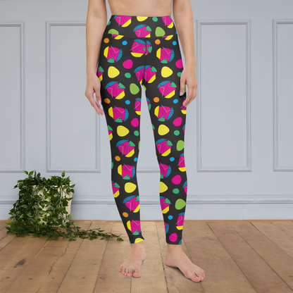 Woman from the waist down wearing high-waist Funk Party funky festival yoga leggings standing facing forwards with her hands by her sides. The woman is standing on a wooden floor with a white panelled wall in the background and a trailing plant on the floor. The funk party pattern  is an abstract pattern in vibrant pink, orange, yellow, green and blue in a spotty type arrangement on a black background