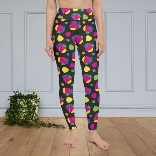 Woman from the waist down wearing high-waist Funk Party funky festival yoga leggings standing facing forwards with her hands by her sides. The woman is standing on a wooden floor with a white panelled wall in the background and a trailing plant on the floor. The funk party pattern  is an abstract pattern in vibrant pink, orange, yellow, green and blue in a spotty type arrangement on a black background