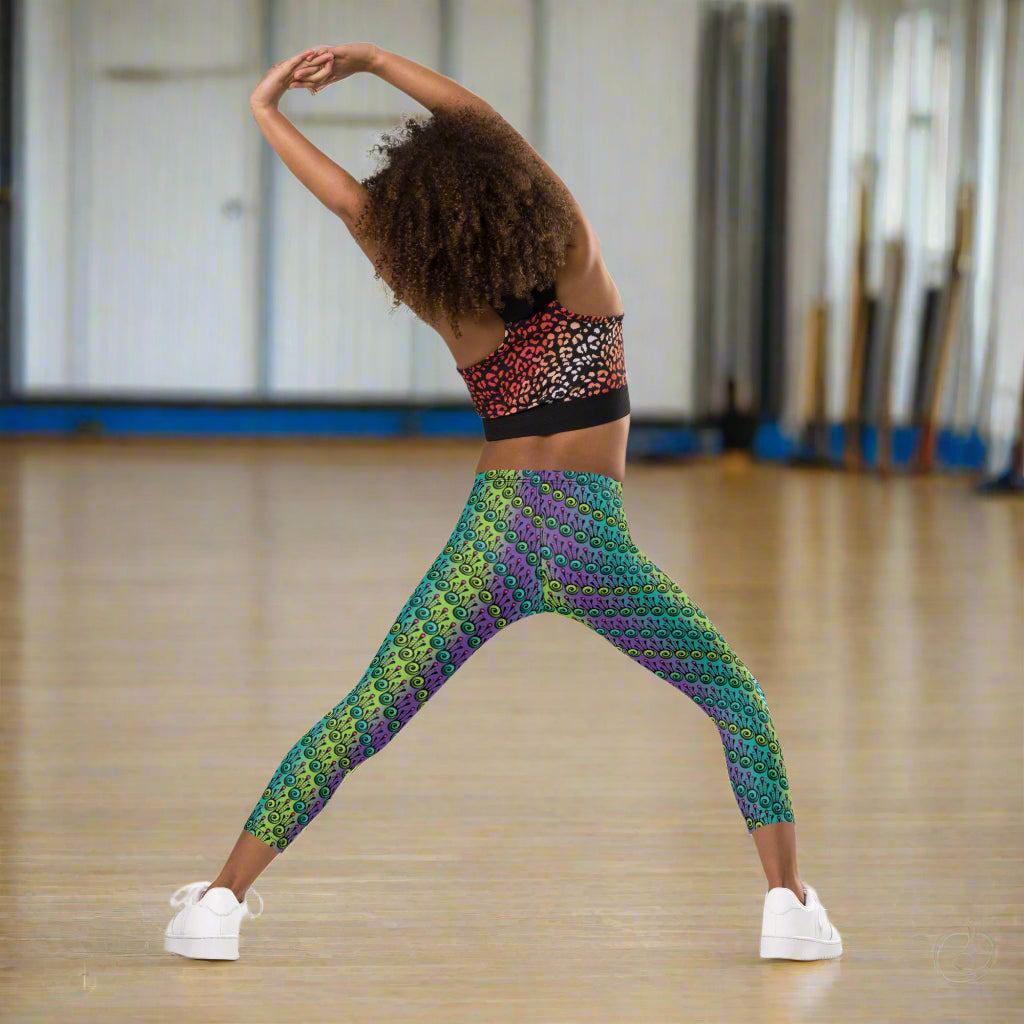 A young girl  poses facing backwards wearing kids size jungle tribal frog funky festival leggings. She is in a brightly lit neutral coloured dance studio. The jungle tribal frog pattern is an abstract pattern with a blended green and purple background.