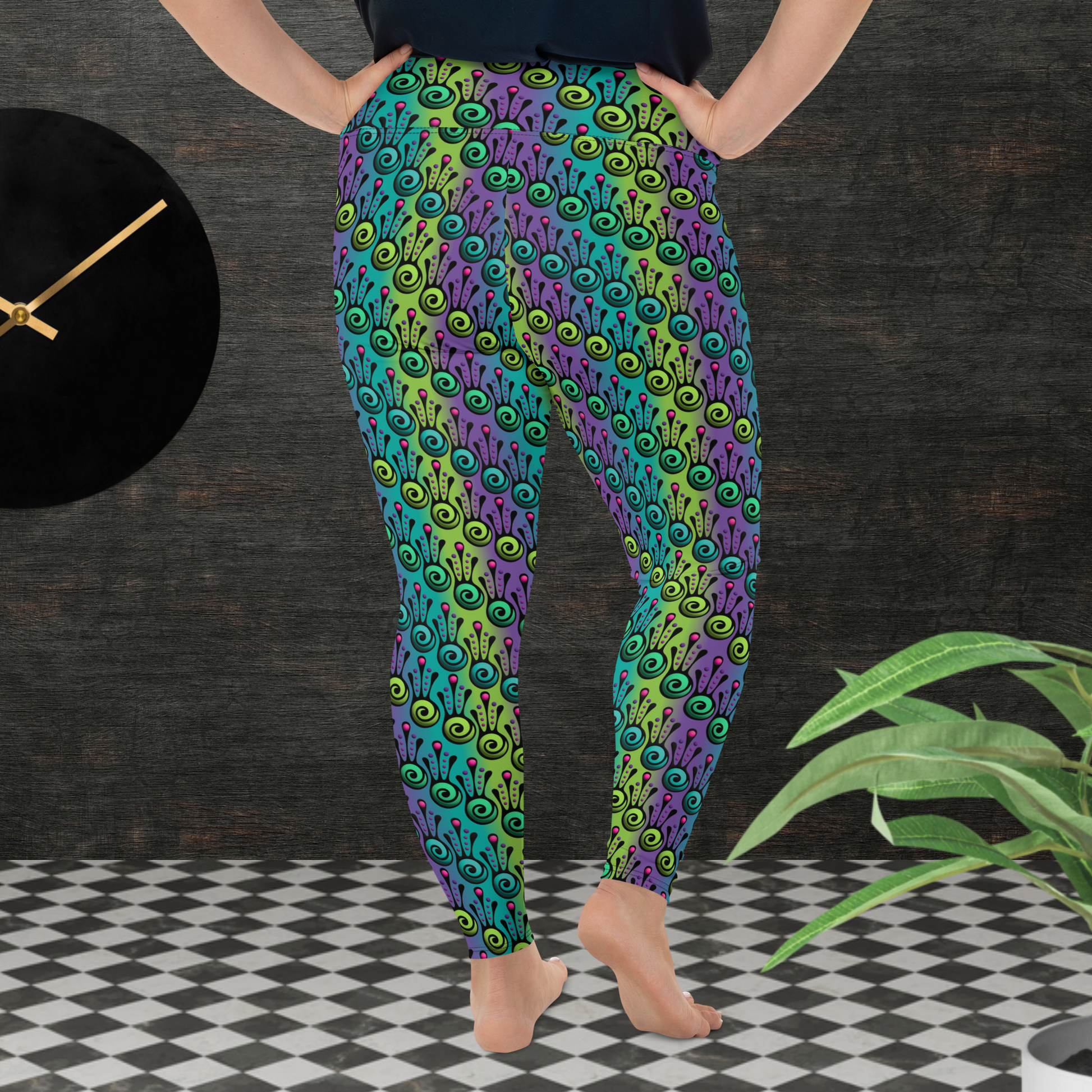 A curvy woman from the waist down wearing plus-size high-waist Tribal Frog funky festival yoga leggings standing facing to the back with both hands on her hips. The woman is standing on a black and white tiled floor in front of a textured grey background with a black and gold wall clock to the left and a partially visible leafy plant on the floor in the bottom right. The jungle tribal frog pattern  is an abstract pattern with a blended green and purple background.