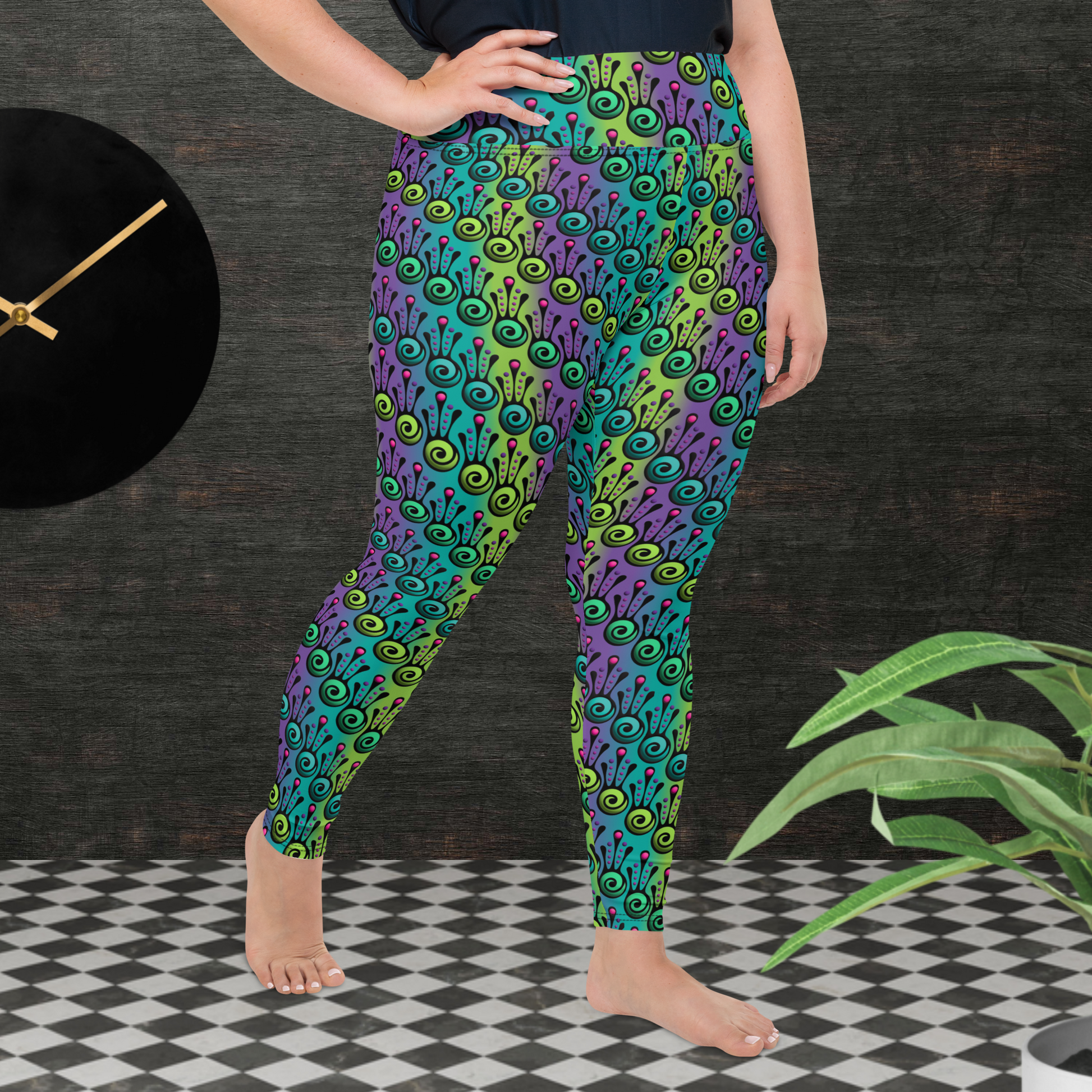 A curvy woman from the waist down wearing plus-size high-waist Tribal Frog funky festival yoga leggings standing facing to the right with her left foot forward and her right hand on her hip. The woman is standing on a black and white tiled floor in front of a textured grey background with a black and gold wall clock to the left and a partially visible leafy plant on the floor in the bottom right. The jungle tribal frog pattern  is an abstract pattern with a blended green and purple background.