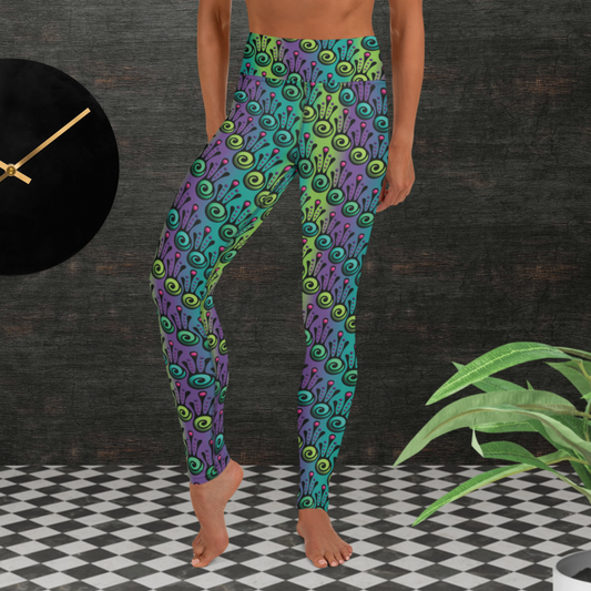 Woman from the waist down wearing high-waist Tribal Frog funky festival yoga leggings standing facing forwards with her hands by her sides. The woman is standing on a black and white tiled floor in front of a textured grey background with a black and gold wall clock to the left and a partially visible leafy plant on the floor in the bottom right. The jungle tribal frog pattern  is an abstract pattern with a blended green and purple background.