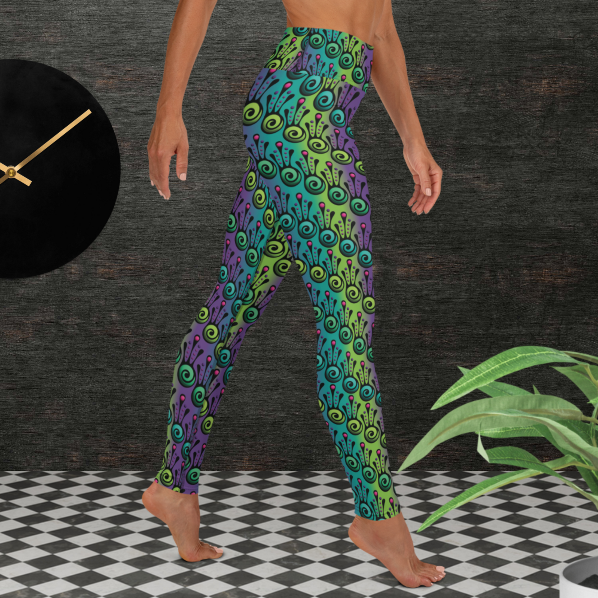 Woman from the waist down wearing high-waist Tribal Frog funky festival yoga leggings standing facing to the right with her right leg forwards and her hands downwards. The woman is standing on a black and white tiled floor in front of a textured grey background with a black and gold wall clock to the left and a partially visible leafy plant on the floor in the bottom right. The jungle tribal frog pattern  is an abstract pattern with a blended green and purple background.