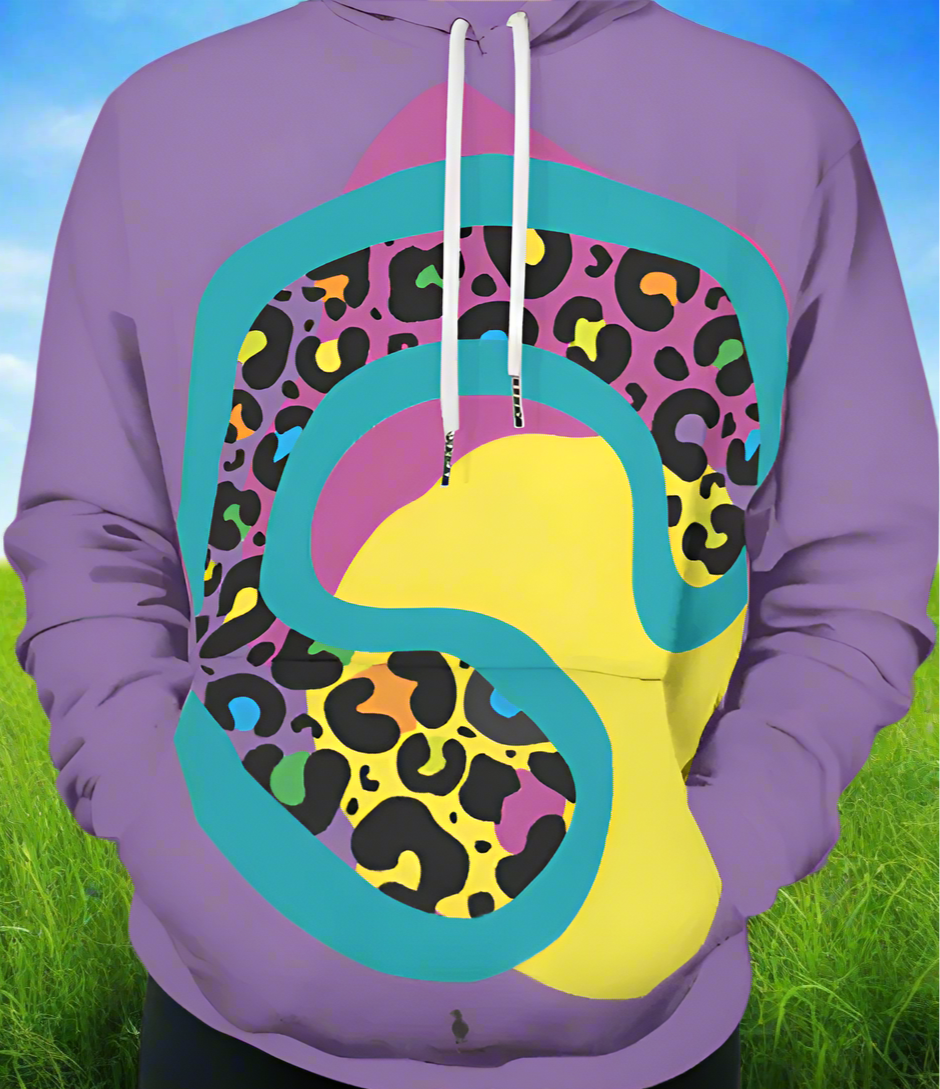 Man from the shoulders down to the waist, posing standing facing forwards wearing a 100% cotton vibrant purple leopard leopard splodge graphic hoodie. He is standing against a grassy background with bright blue sky. The hoodie is purple with a retro rainbow coloured leopard print design covering the front. A large turquoise-green leopard print motif contains lots of smaller leopard print motifs with rainbow coloured centres. This lies on top of large pink and yellow 
