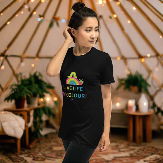 Woman wearing a black 100% cotton vibrant, rainbow live life in colour t-shirt in a bohemian yurt interior decorated with fairy lights, rugs, candles and plants.